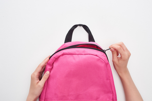 Partial view of schoolgirl zipping bright pink schoolbag isolated on white - Photo, Image