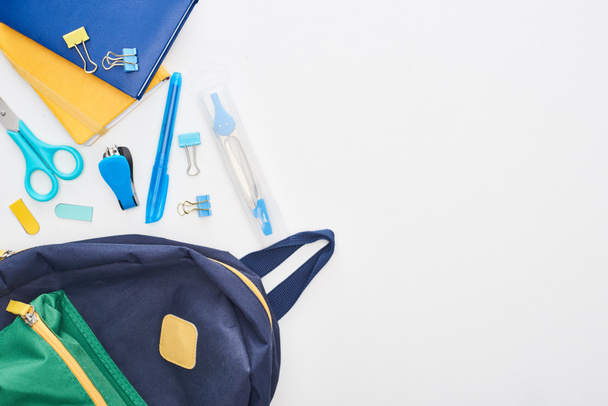 Sininen koululaukku lähellä lehtiöitä, sakset ja eri koulutarvikkeet eristetty valkoinen
  - Valokuva, kuva