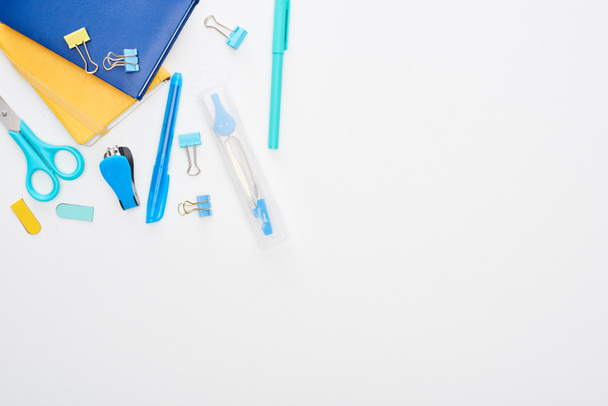 Top view of blue scattered school supplies near notepads isolated on white - Foto, Imagem