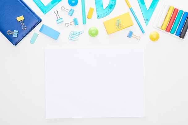 Vue du dessus des fournitures scolaires dispersées bleues et jaunes avec bloc-notes près du papier clair isolé sur blanc
 - Photo, image