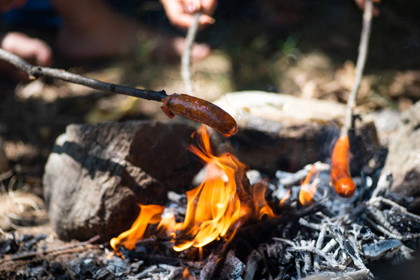 Les gens qui cuisinent des saucisses en feu pendant un pique-nique
 - Photo, image