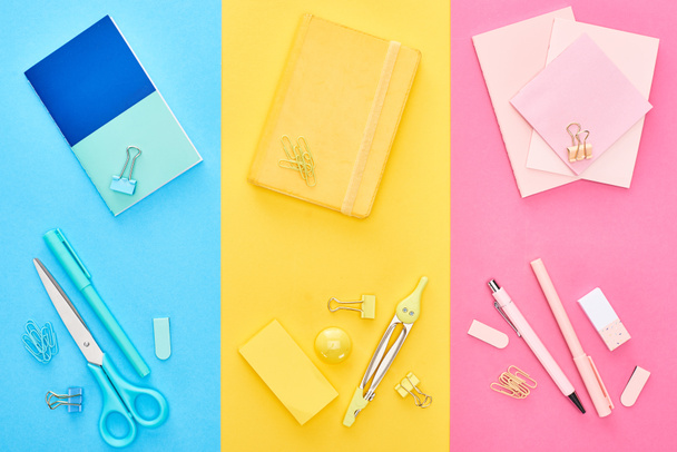 Top view of yellow and blue notepads near pink sheets of paper with different stationery on tricolor background - Foto, Imagen