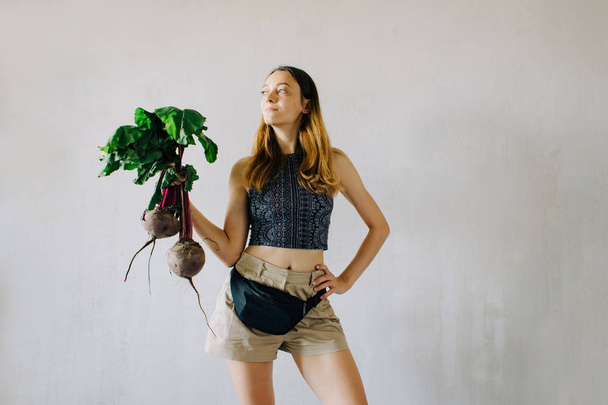 young pretty girl holding fresh organic beet on grey background - Fotografie, Obrázek