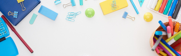Panoramic shot of blue and yellow scattered school supplies and cup with colorful felt-tip pens isolated on white - Photo, Image