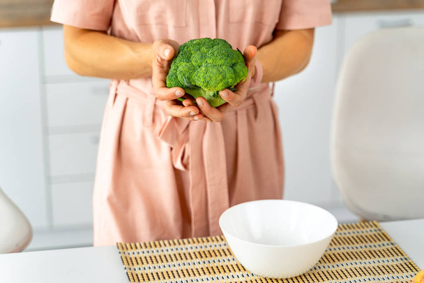Young happy woman holding broccoli in the beautiful kitchen. Healthy food and Dieting concept. Loosing Weight - Fotó, kép