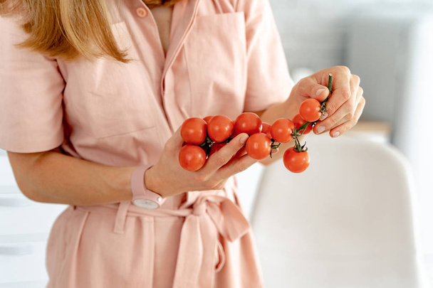 Woman holding branch of ripe cherry tomatoes, closeup - Photo, Image