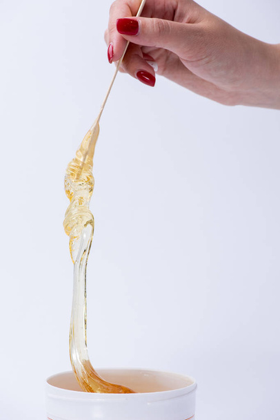 flüssige gelbe Zuckerpaste oder Wachs zum Enthaaren auf einem Stick in der Nähe - Foto, Bild