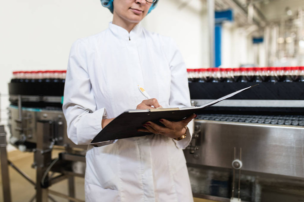 Trabajadora en fábrica de embotellado revisando botellas de jugo antes del envío. Control de calidad de la inspección
.  - Foto, Imagen