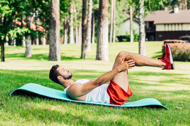 Zijaanzicht van sportman met gesloten ogen doen ABS op fitness mat buiten  - Foto, afbeelding