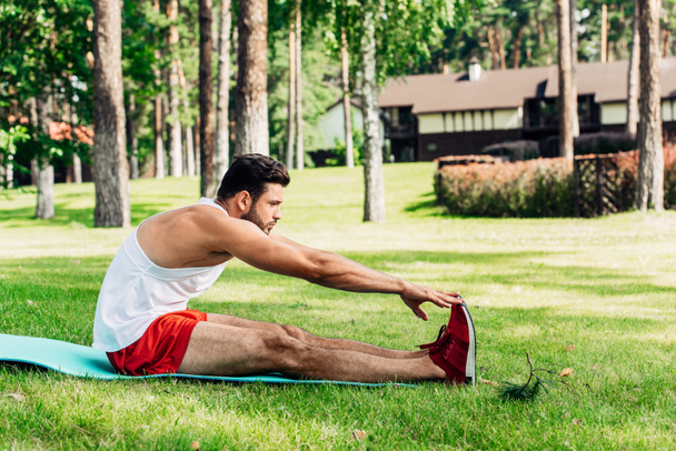 προφίλ του όμορφος αθλητής κάνει τέντωμα άσκηση στο χαλάκι γυμναστικής  - Φωτογραφία, εικόνα