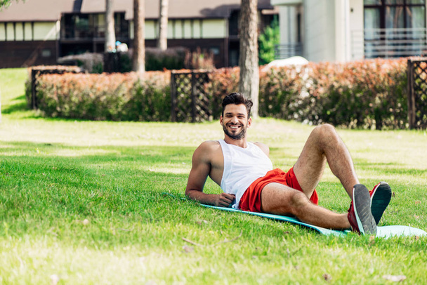 芝生の外のフィットネスマットに横たわっている陽気な男の選択的な焦点 - 写真・画像