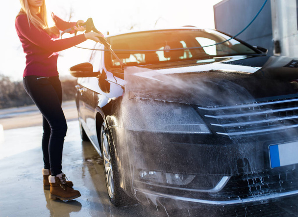 Молодая женщина моет автомобиль с микроволоконной тканью, детализирует автомобиль (или камердинер) концепция
.  - Фото, изображение