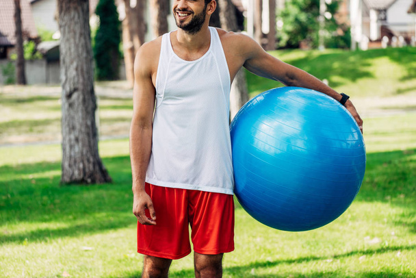 oříznutý pohled veselého sportovce, který drží modrý fitness Ball  - Fotografie, Obrázek