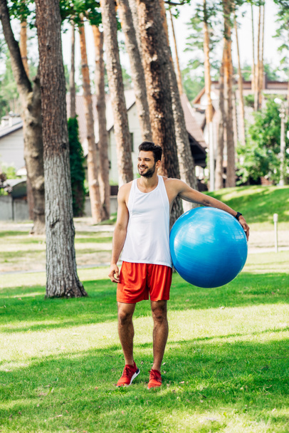 sportif joyeux debout sur l'herbe verte et tenant ballon de fitness bleu
  - Photo, image
