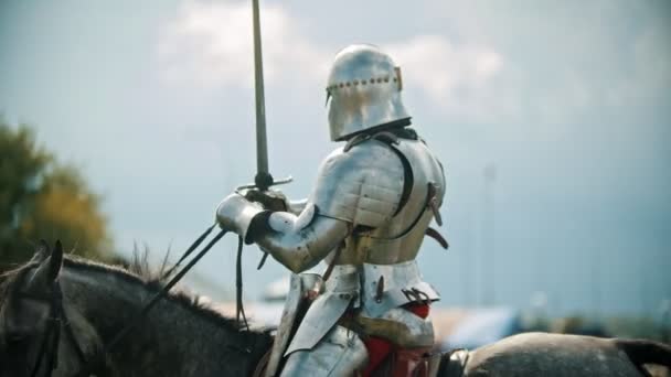 Un caballero montando un caballo alrededor del campo de batalla y saludando a la gente mirando detrás de la valla levanta la mano en el cielo sosteniendo una espada
 - Metraje, vídeo