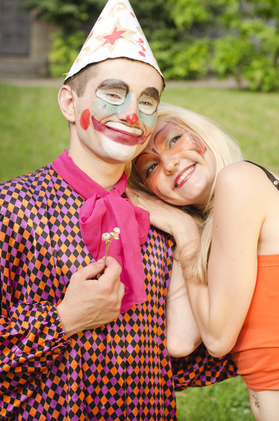 Porträt eines lächelnden Mannes, der wie ein Clown mit einer Blume für ein glückliches Mädchen mit Schmetterling-Make-up gekleidet ist - Foto, Bild