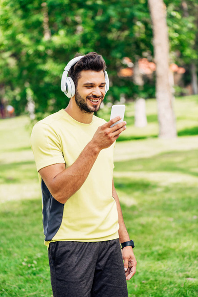 happy bearded man looking at smartphone and listening music in headphones - Photo, Image