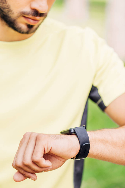 cropped view of bearded man looking at fitness tracker outside  - Photo, Image