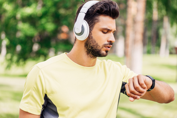 schöner bärtiger Mann mit Kopfhörer schaut Fitness-Tracker an  - Foto, Bild