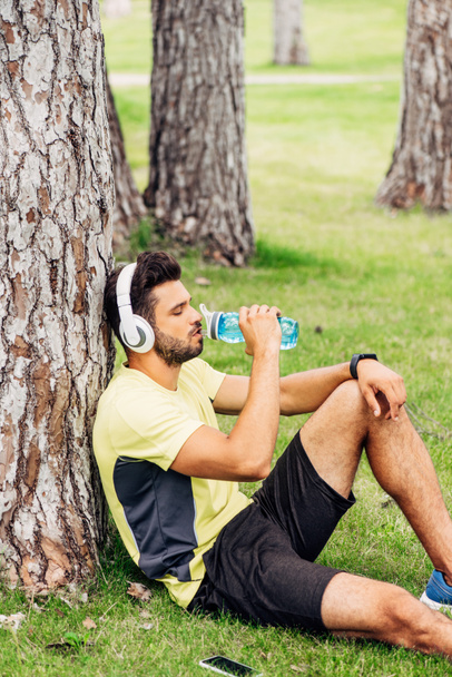 komea urheilija kuulokkeet juomaveden lähellä puunrunko
  - Valokuva, kuva