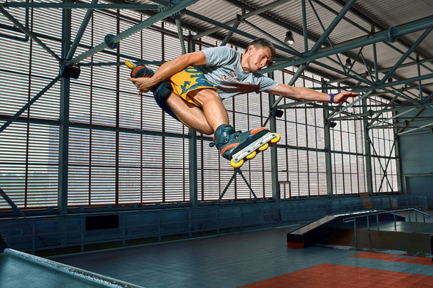 Rollerblader sauter haut de la grande rampe d'air performant tour. Équipement de skate park intérieur
. - Photo, image