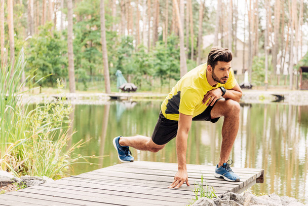 handsome bearded man in sportswear exercising near lake in forest  - Zdjęcie, obraz