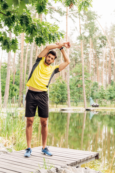 handsome bearded sportsman exercising near lake in forest  - Foto, Imagen