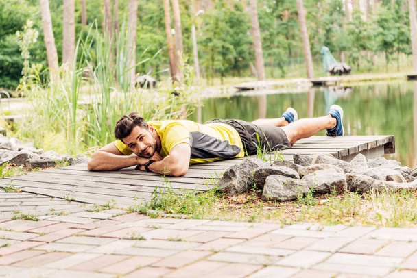 selective focus of athletic man in sportswear lying near lake in forest  - Foto, imagen