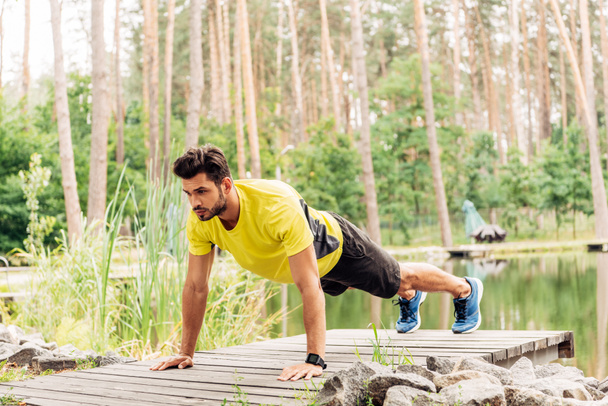 athletic man in sportswear doing press ups near lake in forest  - Photo, Image