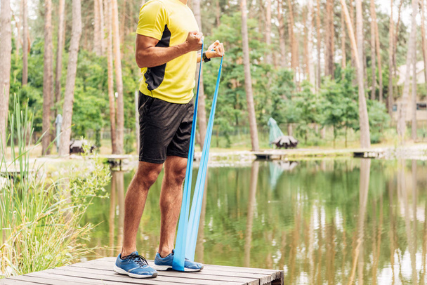 cropped view of sportsman exercising with suspension straps near lake  - Valokuva, kuva