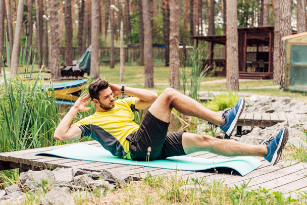  handsome sportsman training on fitness mat near stones and trees  - Zdjęcie, obraz
