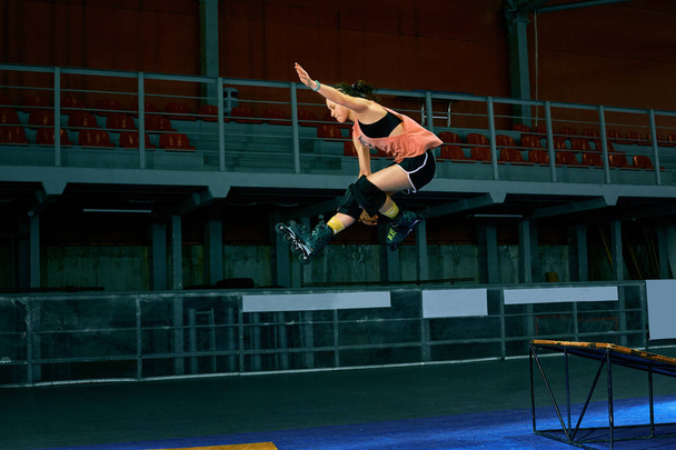 Rollerblader jump high from big air ramp performing trick. Indoors skate park equipment. - Fotó, kép