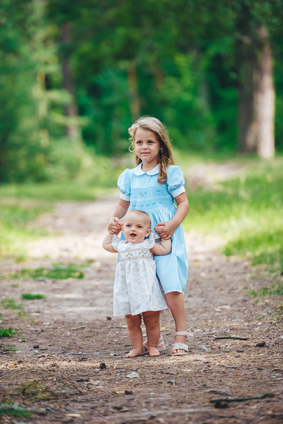 Dos monas hermanas jóvenes jugando en el soleado parque de verano y tomados de la mano
.  - Foto, imagen