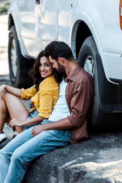 handsome and bearded man with closed eyes sitting near car with attractive woman  - Фото, зображення