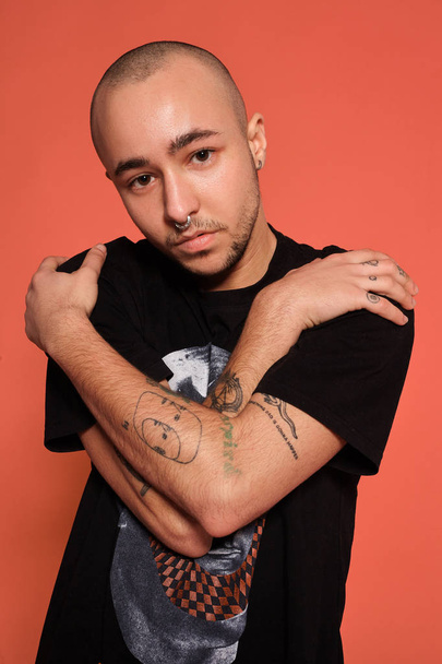 Studio-kuva nuoresta tatuoidusta kaljusta miehestä poseeraamassa vaaleanpunaista taustaa vasten. 90-luvun tyyli
. - Valokuva, kuva