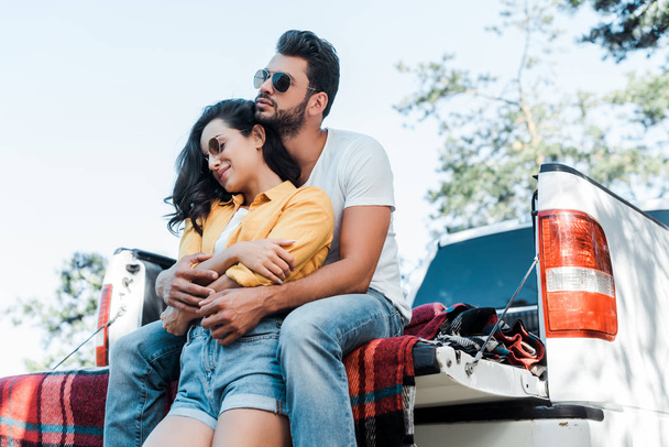 handsome man hugging beautiful girl in sunglasses near car  - Fotografie, Obrázek