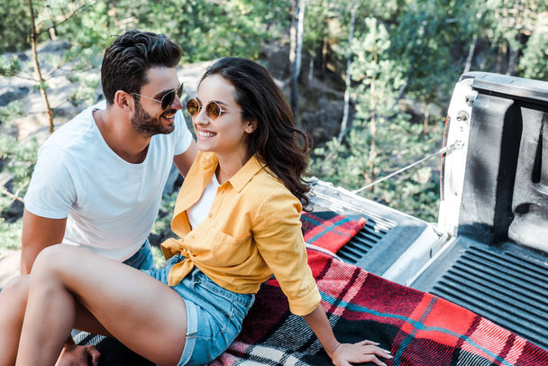 happy bearded man smiling with young woman sitting on blanket in summertime  - Foto, Imagen