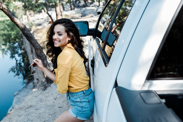selectieve focus van vrolijk meisje met zonnebril in de buurt van auto  - Foto, afbeelding