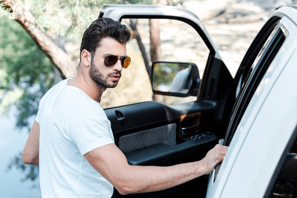 вибірковий фокус бородатого чоловіка в сонцезахисних окулярах, що стоять біля автомобіля
  - Фото, зображення