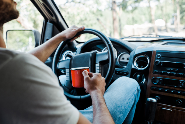 cropped view of bearded man holding cup and touching steering wheel  - Photo, image