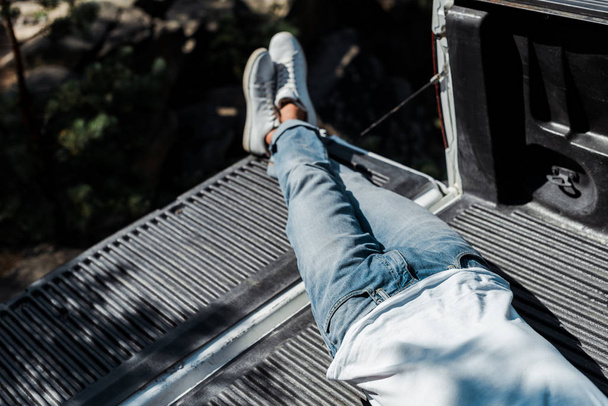 overhead view of man lying in blue denim jeans in car trunk  - Photo, Image