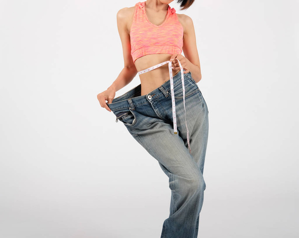 sporty fitness woman in loose jeans after losing weight on white - Foto, imagen