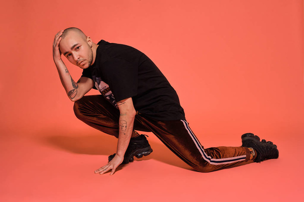 Studio shot of a young tattoed bald man posing against a pink background. 90s style. - Foto, afbeelding