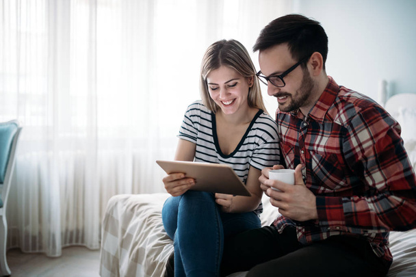 Young happy couple using digital tablet in bedroom - Fotoğraf, Görsel