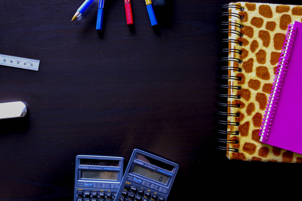 Komposition von Büroobjekten bestehend aus zwei Notizbüchern mit zwei Taschenrechnern, Stiften und einem Textmarker auf schwarzem Hintergrund von oben betrachtet - Foto, Bild