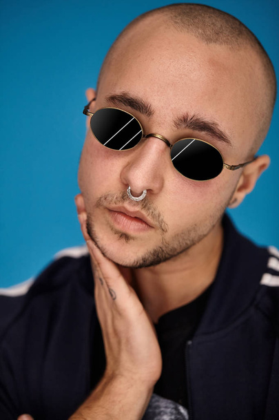 Studio shot of a young tattoed bald man posing against a blue background. 90s style. - Photo, image