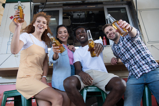 low angle view of happy multicultural friends holding  bottles with beer near food truck   - Photo, Image