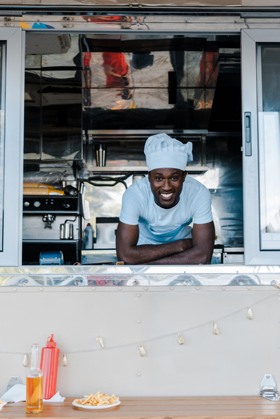 Gelukkig African American man in chef uniform glimlachend van Food truck  - Foto, afbeelding