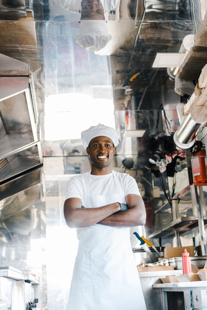 alegre afroamericano chef de pie con brazos cruzados en camión de comida
  - Foto, Imagen