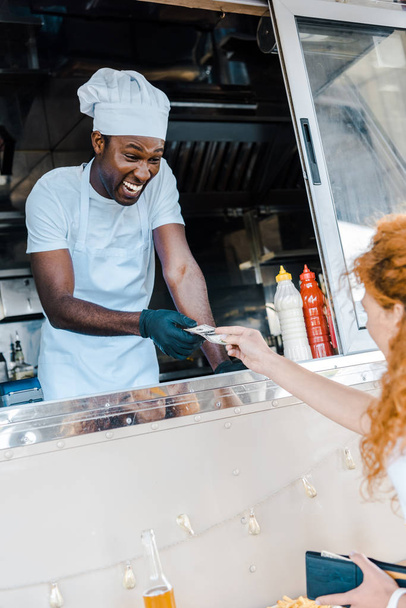 selective focus of redhead girl giving cash to happy african american man in food truck  - Foto, Bild